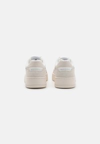 Weiße Wildleder-Low-Top-Sneaker mit einem glatten Design, gepolstertem Kragen und geprägtem Logo an der Ferse, minimalistisches ästhetisches Erscheinungsbild.