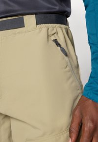 Shorts beiges en tissu texturé, avec une poche latérale zippée et une taille élastique. Coutures détaillées le long des seams.