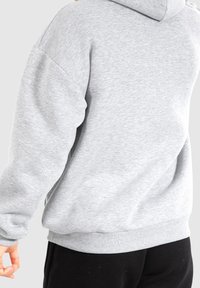 Sweat à capuche gris, coupe ample, tissu doux, poignets et ourlet côtelés, design minimaliste, coutures visibles, sans motifs ni logos.