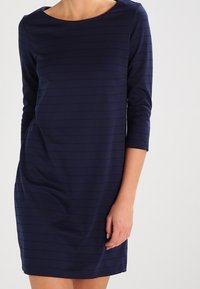 Robe bleu marine à manches trois-quarts, avec de subtiles rayures horizontales, un col rond et une coupe décontractée.