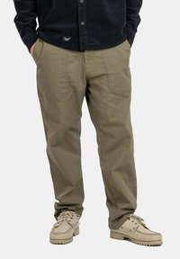 Pantaloni cargo color khaki con una finitura testurizzata, dotati di due tasche frontali e un fit rilassato, abbinati a scarpe beige con lacci.