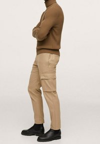 Pantalon cargo beige en tissu léger avec des poches latérales, associé à un col roulé côtelé marron et des bottines noires.