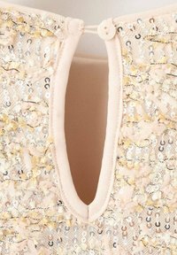 Różowobrązowy strój z okrągłym dekoltem i ozdobnym otworem na plecach, zdobiony cekinami i fakturowanymi aplikacjami.