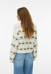 Pull en tricot avec une base vert clair, décoré de motifs floraux en rose et vert foncé. Couleur oversize, poignets et ourlet côtelés.