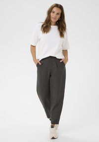 Witte top met korte mouwen en een boot-halslijn, gecombineerd met hoog-waist, donkergrijze geplooide broeken. Het model draagt lichte sneakers.