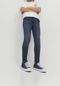Jeans skinnies de mezclilla azul oscuro con un ligero desvanecimiento, combinados con una camiseta blanca y zapatillas de lona navy con suelas y cordones blancos.