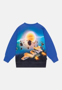 Modrý a černý svetr s živou scénou z vesmíru, na které je kosmická loď létající mezi asteroidy směrem k zářícímu slunci.