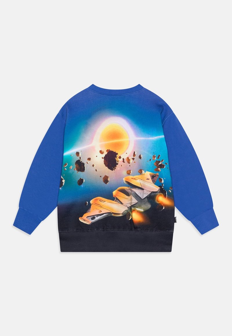 Modrý a černý svetr s živou scénou z vesmíru, na které je kosmická loď létající mezi asteroidy směrem k zářícímu slunci.