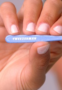 Lime à ongles bleue de Tweezerman avec une texture lisse, arborant un logo blanc. Tenue entre des doigts avec des ongles naturels de couleur claire visibles.