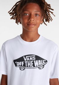 Vit bomull t-shirt med en stor svart "Vans Off The Wall" logotyp tryckt i en djärv, lekfull stil på framsidan.
