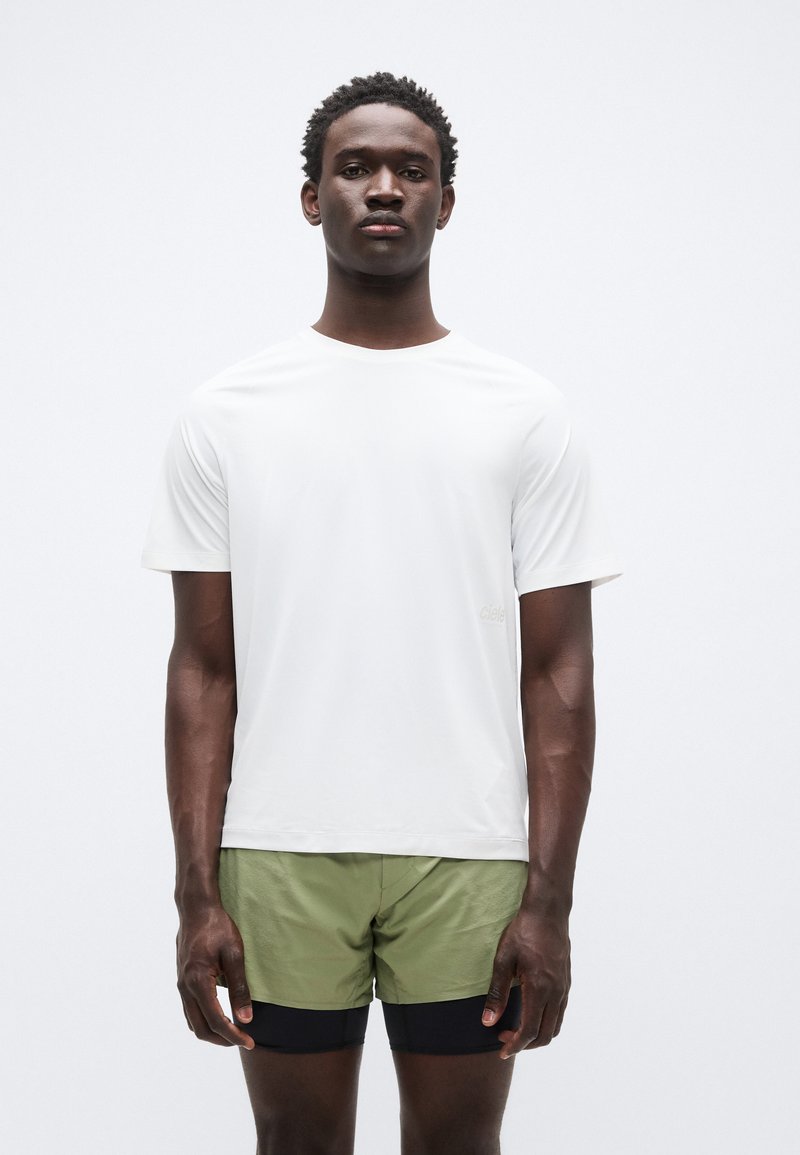 Λευκό κοντομάνικο μπλουζάκι από ελαφρύ ύφασμα, σε συνδυασμό με πράσινα σορτς. Διαθέτει διακριτικό λογότυπο στο μπροστινό μέρος.