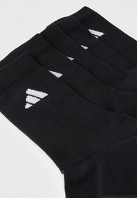 Fekete atlétikai zoknik bordázott textúrával; fehér háromszög alakú logóval; ízlésesen egymásra rendezve, hogy több pár látható legyen.