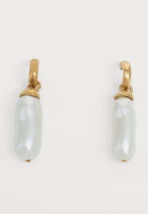 Boucles d'oreilles créoles en or avec des perles blanches allongées suspendues sur un fond clair uni.