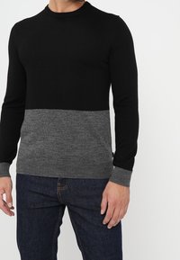 Schwarzer und grauer Strickpullover mit Rundhalsausschnitt, der ein kontrastierendes horizontales Farbblockdesign und gerippte Bündchen aufweist.