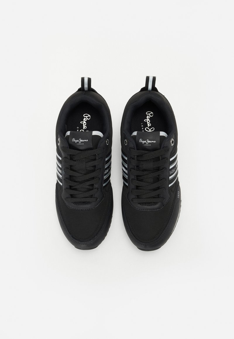 Chaussures de sport noires avec une tige en tissu texturé, présentant des rayures blanches et grises et un col rembourré. Lacets et œillets pour un maintien sécurisé.
