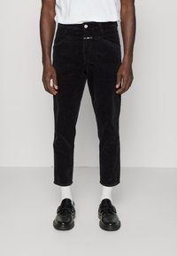 Svarta manchesterbyxor med slim fit, femfickorsdesign och knäppning, matchade med svarta skor och vita strumpor.