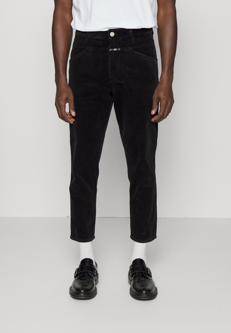 Svarta manchesterbyxor med slim fit, femfickorsdesign och knäppning, matchade med svarta skor och vita strumpor.