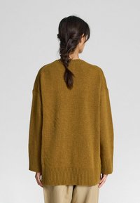 Sennepsgulfarvet oversized strikket sweater med ribbede manchetter og kant, der har en rund halsudskæring og et blødt, struktureret stof.
