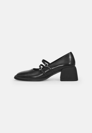 Chaussures Mary Jane en cuir noir avec deux brides réglables, bout rond et talon rectangulaire épais. Texture lisse avec des détails de design discrets.