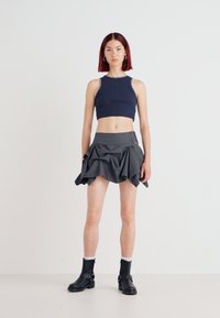 Top cropped em malha azul-marinho com costura prateada, combinado com uma saia plissada cinza. A modelo usa botas de cano corto pretas e meias brancas.