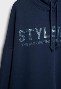 Navy plava majica s kapuljačom ukrašena cirkonima koji tvore riječi "STYLED" i "THE ART OF BEING", s kapuljačom na vezanje i rebrastim manžetama.