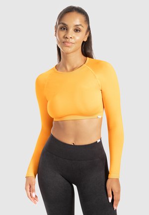 Crop top arancione a maniche lunghe realizzato in un tessuto liscio e elasticizzato con scollatura arrotondata, abbinato a leggings neri a vita alta.