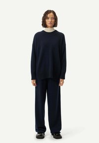 Marinblå oversized stickad tröja med ribbad nederkant, matchad med vida byxor och svarta skor, mot en neutral bakgrund.