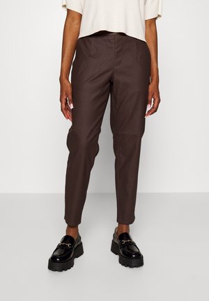 Braune, taillierte Hosen mit Seitentaschen, glattem Stoff und figurnahem Schnitt. Kombiniert mit glänzenden schwarzen Slippern mit einer Kettenakzent.
