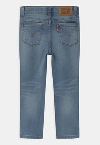 Jean en denim bleu clair avec une coupe droite, des poches arrière, et un patch en cuir marron sur la ceinture avec le logo de la marque.
