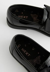 Chaussures en cuir verni noir avec une semelle plate, ornées d'un nœud décoratif et d'un intérieur à motifs avec un design de papillon et des étoiles.