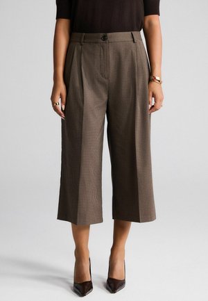 Braun karierte hochtaillierte Culottes mit Falten, Knopfverschluss und seitlichen Taschen, kombiniert mit spitzen braunen Absätzen.