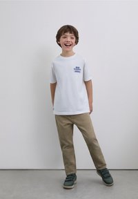White T-shirt with blue print, tan pants, and green sneakers. The shirt has short sleeves and a round neckline.