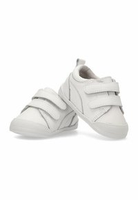 Zapatillas infantiles blancas de material sintético con una textura suave. Cuentan con dos correas de velcro y detalles plateados en los laterales.