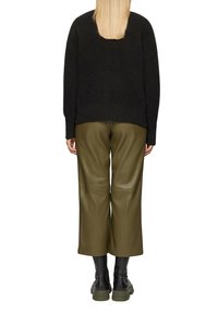 Schwarzer Strickpullover, olivgrüne, lederne, cropped Hose und schwarze Stiefeletten mit dicken Sohlen, von hinten betrachtet.