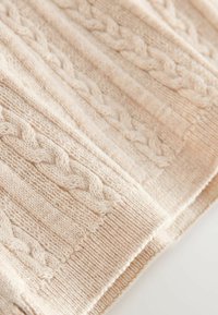 Beige gestrickter Stoff mit strukturierten Zopfmuster und gerippten Bereichen. Weiche, gemütliche Textur mit subtilen Farb- und Tiefenvariationen.