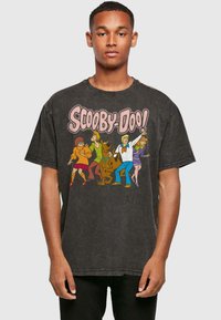 Camiseta negra de corte oversize hecha de algodón con una impresión gráfica de los personajes de Scooby-Doo en colores brillantes en el frente.
