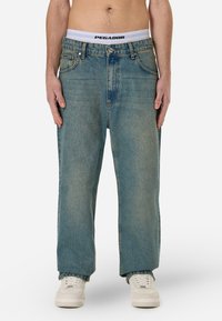 Heledad sinine teksapüksid, millel on lõtv sirge lõige, viis taskut ja nööpidega lukustus. Ühendatud valge talje ja spordijalatsitega.