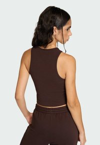 Hnedý rebrovaný krátky top s vysokým výstrihom a bez rukávov, v kombinácii s vysokými pásovými nohavicami zhodnej farby. Hladká textúra.