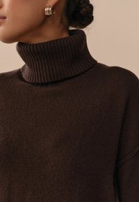 Brauner Rollkragensweater aus strukturiertem Strickstoff mit hohem geripptem Kragen. Hat einen lockeren Schnitt und eine weiche Optik.
