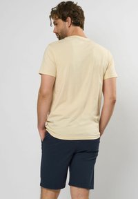 Tricou cu mânecă scurtă, de culoare bej deschis, confecționat dintr-un material moale, cu un guler rotund și o croială lejeră, asortat cu pantaloni scurți în nuanță de albastru marin.