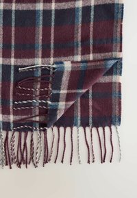 Burgundia, tumesinine ja kreemjas karvane tekk frillide äärtega. Pehme tekstuur, kudum kangas, silmapaistvad diagonaalsed triibud ja ruuduline muster.