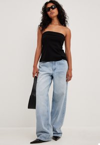 Haut noir sans bretelles associé à un jean large bleu clair. La modèle tient un sac à main noir et porte des lunettes de soleil sombres. Texture lisse dans l'ensemble.