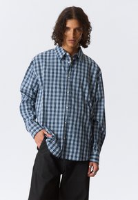 Overhemd met knopen in een marineblauw en wit ruitpatroon, lange mouwen, relaxte pasvorm, met een klassieke kraag en een afgeronde zoom.