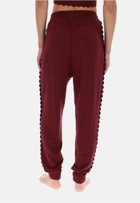 Burgundy smalle joggers med en tekstureret, bølget sidelomme og elastik i taljen. Fremstillet af blødt, åndbart stof.