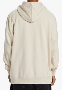 Světlý béžový mikina s kapucí vyrobená z měkkého materiálu, s volným střihem, žebrovanými manžetami a velkým středovým švem na zádech.