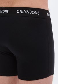 Black boxer shorts made of stretch fabric featuring a black waistband with "ONLY & SONS" logo in white. Smooth texture, form-fitting design.