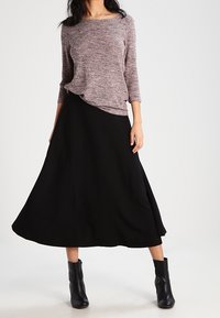 Jasnobrązowy sweter o fakturze, z rękawami trzy czwarte, zestawiony z zwiewną czarną midi spódnicą. Czarne botki za kostkę dopełniają całość.