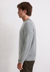 Szary dzianinowy sweter z klasycznym okrągłym dekoltem i długimi rękawami, z ribbowanymi mankietami i dołem, prezentowany na modelu z boku.