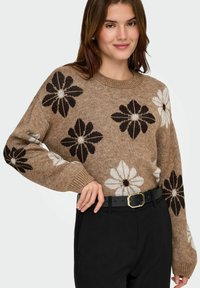 Suéter de punto en marrón con grandes patrones florales en negro y blanco. Cuenta con un cuello redondo y puños acanalados. Se complementa con un cinturón negro.