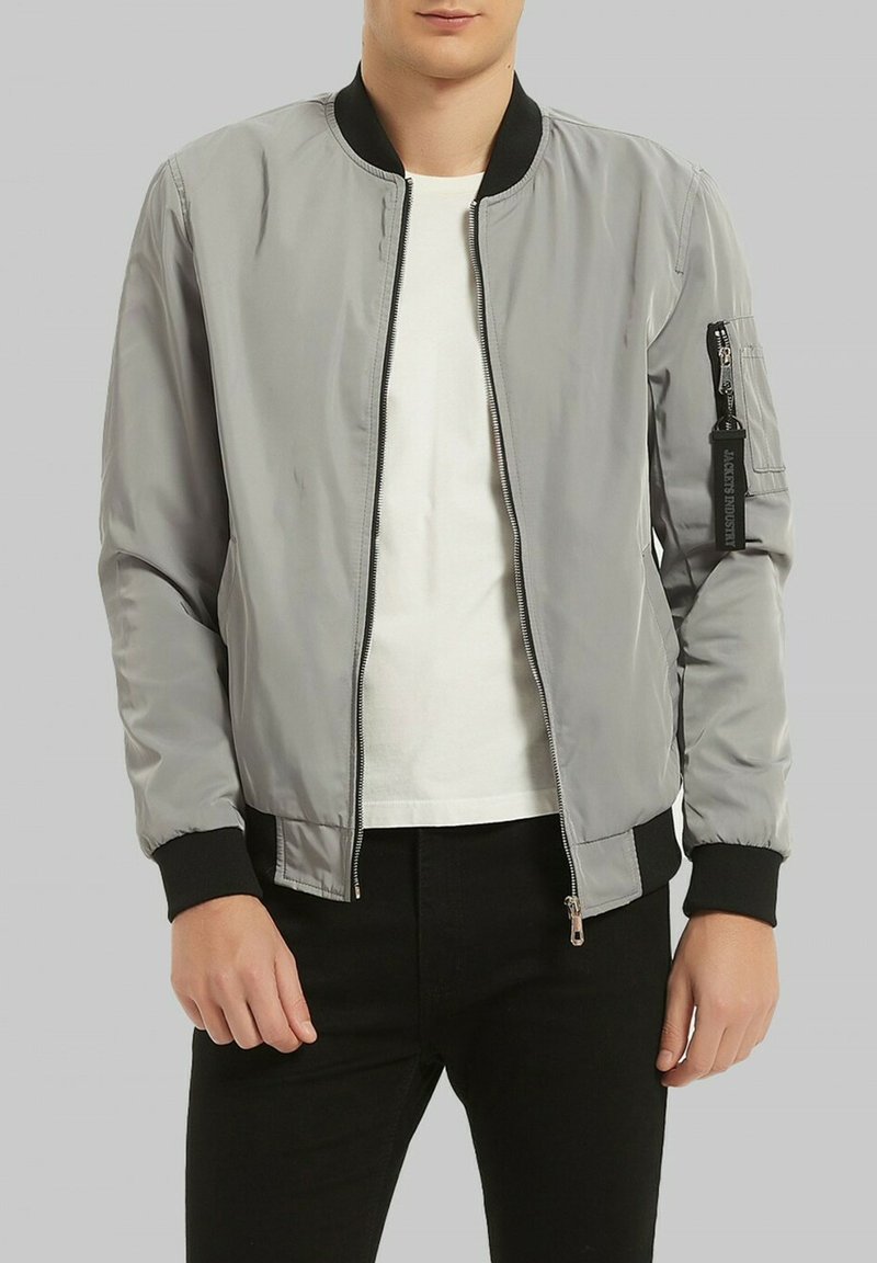 Veste bomber grise avec fermeture éclair à l'avant, col et poignets côtelés noirs, poches latérales et poche zippée sur la manche gauche.